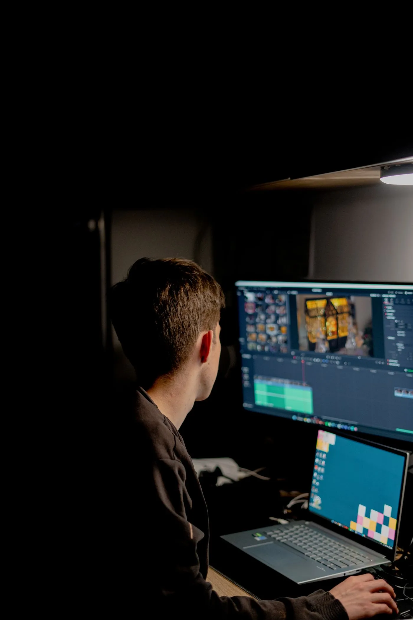 An editor cutting a film on a dual-screen setup in a dark room
