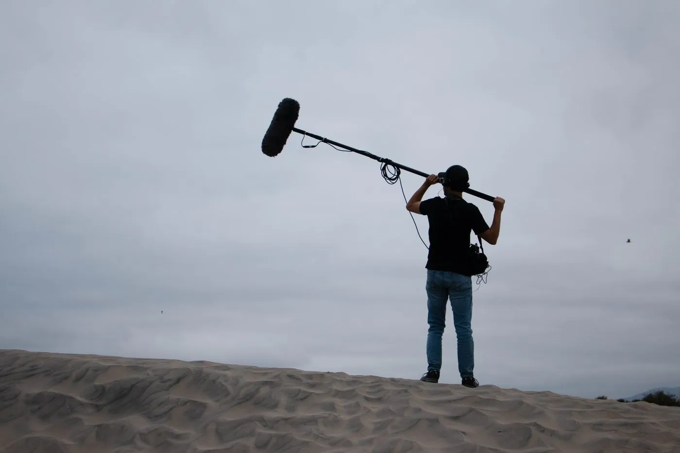 A sound technician holding a boom microphone on a sandy dune