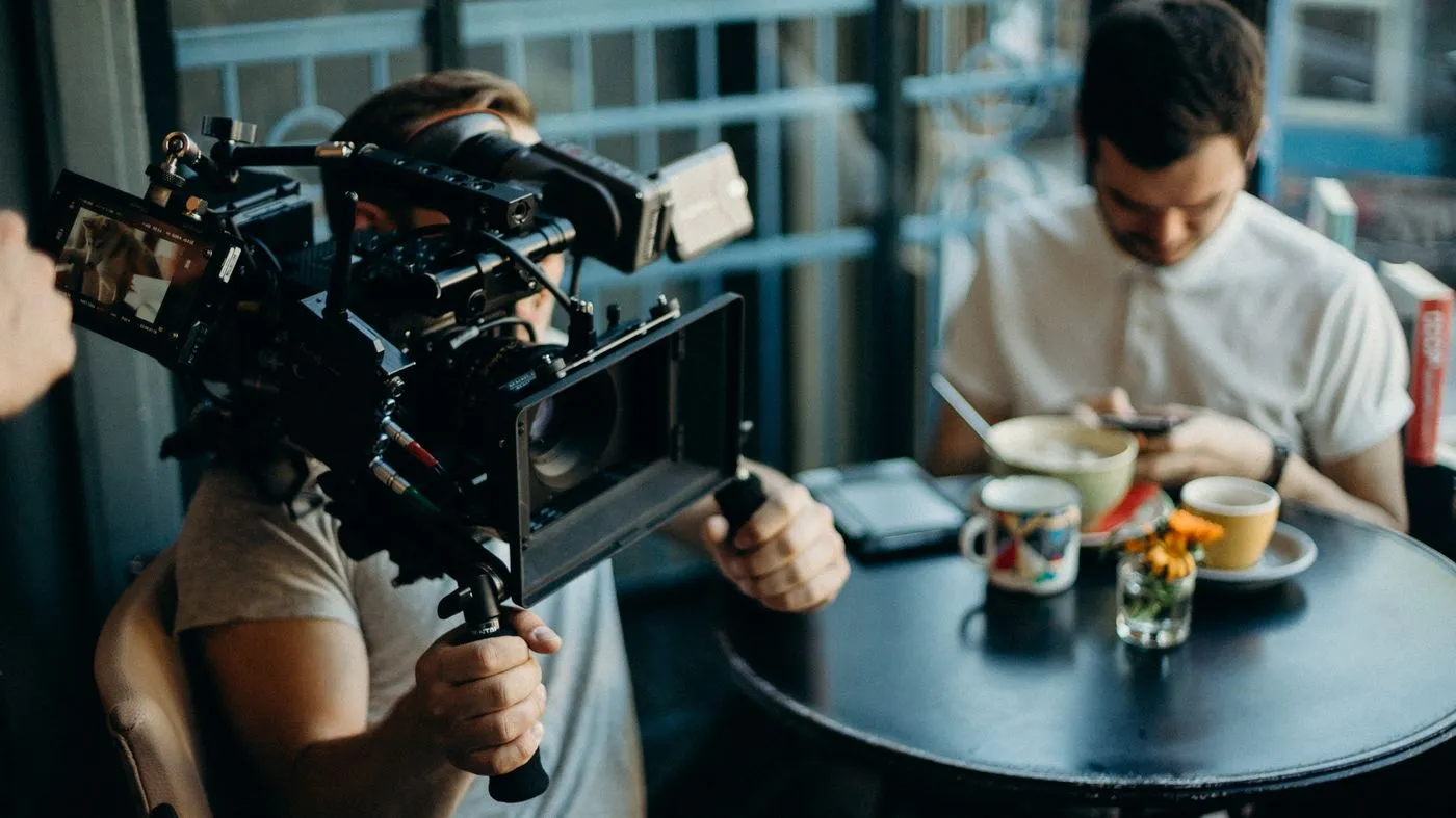 Two filmmakers adjusting camera equipment indoors on a shoot