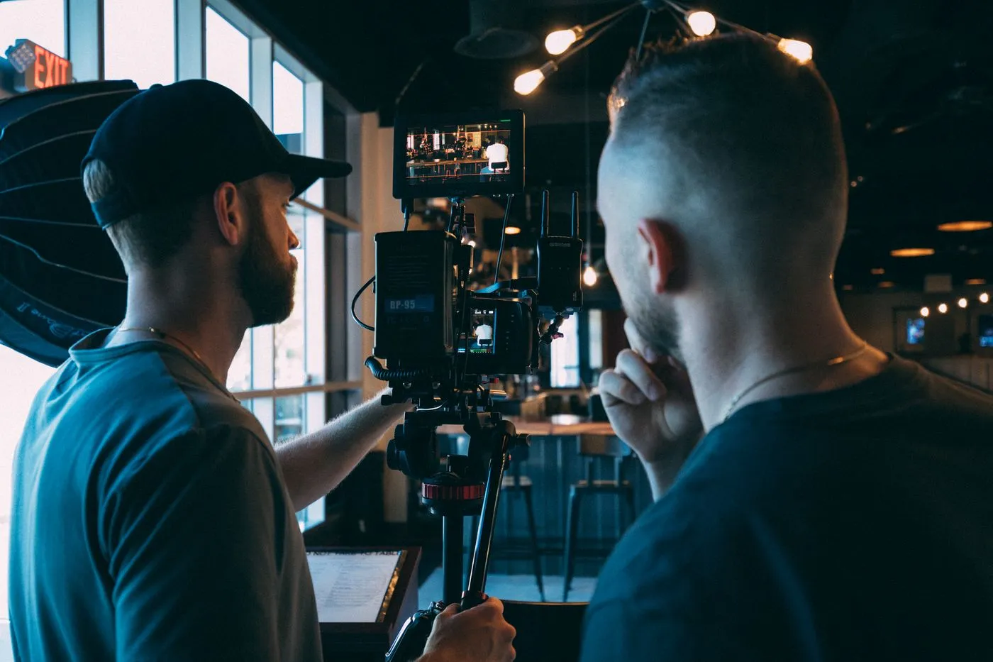 Two filmmakers adjusting camera equipment indoors on a shoot