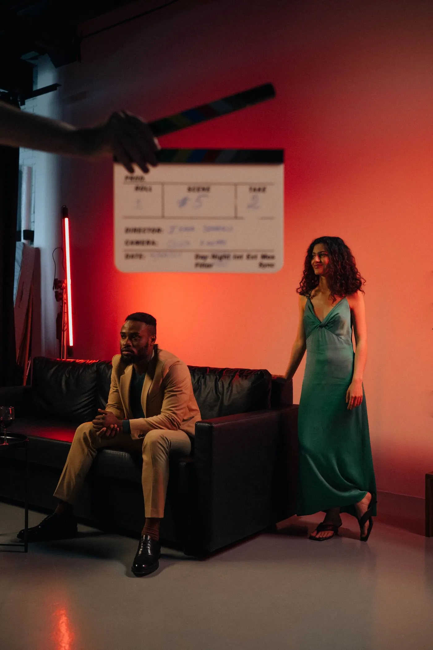 Two actors on a set lit with deep red light beside a clapperboard